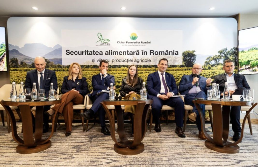 Panel of six professionals seated in armchairs during a conference, with a banner behind them reading 'Securitatea alimentară în România' and a rural landscape backdrop. The table in front holds water bottles and microphones.] ,