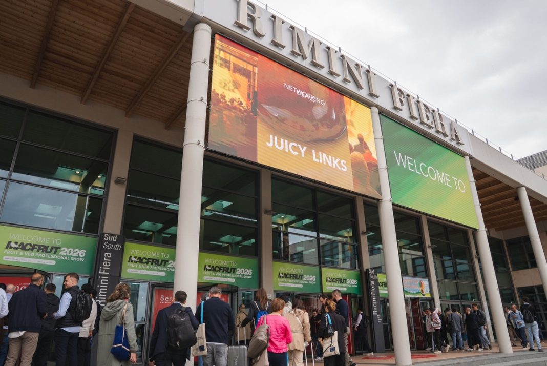 People queue outside Rimini Fiera at a convention center entrance beneath a large 'Juicy Links' banner and a green 'Welcome To' sign.