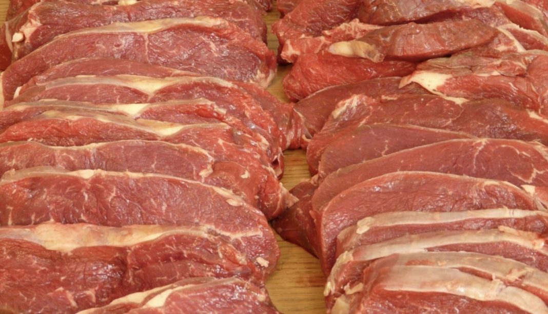 Rows of raw beef steaks arranged on a wooden surface, showing marbling and fat edges.