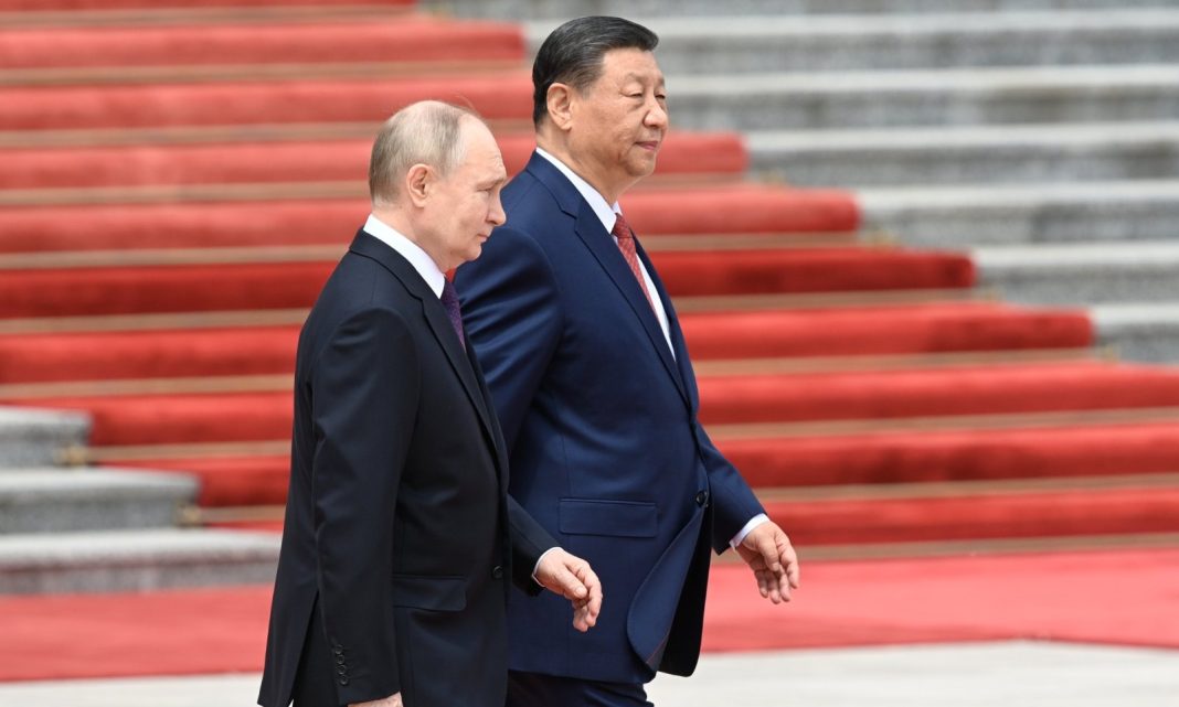 Two men in dark suits walking side by side on a red-carpeted staircase, seen from the side in a formal setting.