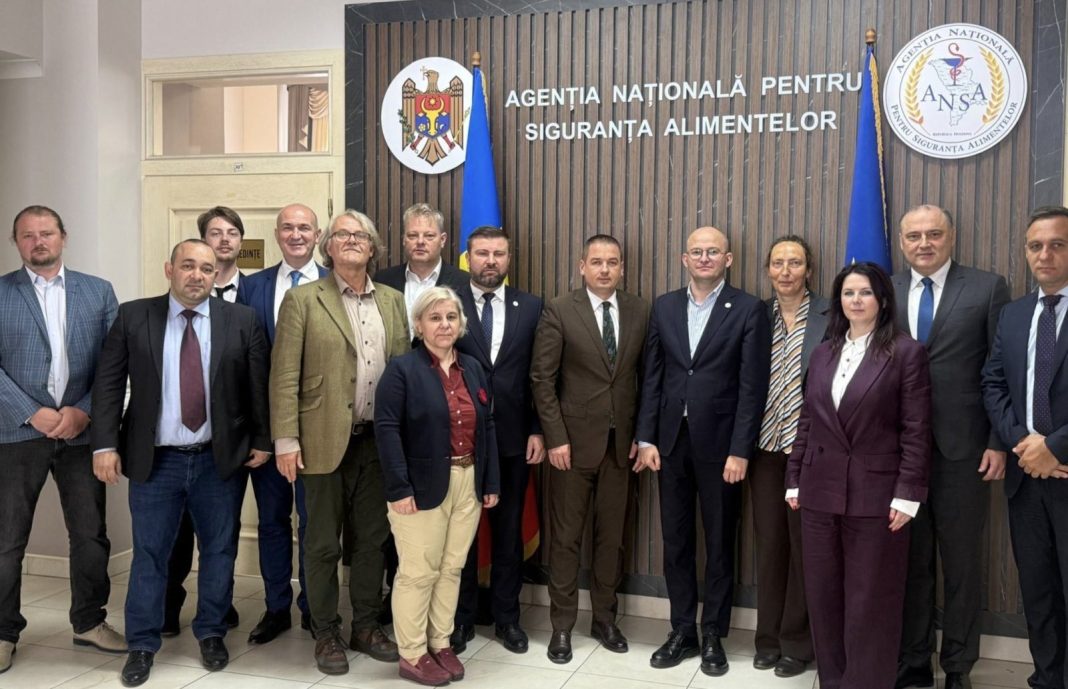 Group of officials in business attire posing for a formal photo in front of the Agency for Food Safety sign (Agenția Națională pentru Siguranța Alimentelor).