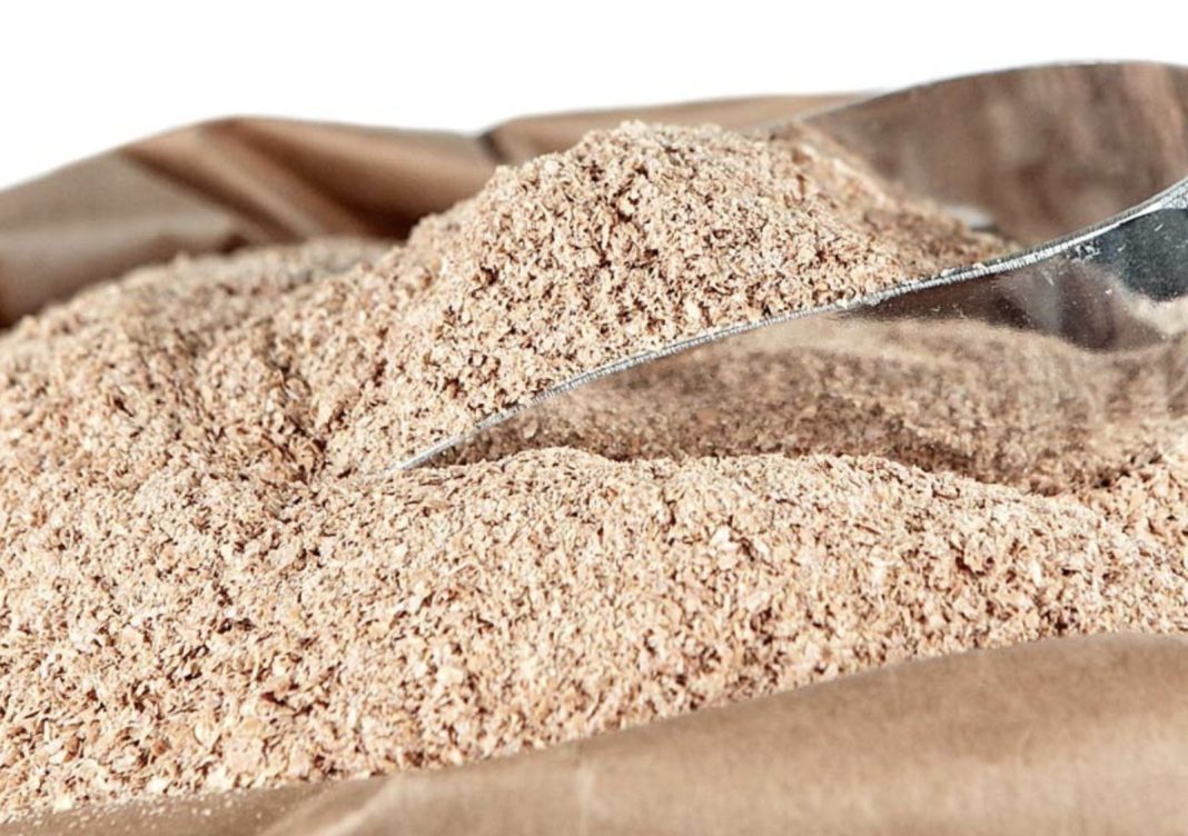 Ground cinnamon spilling from a metal scoop onto a brown paper bag, close-up view