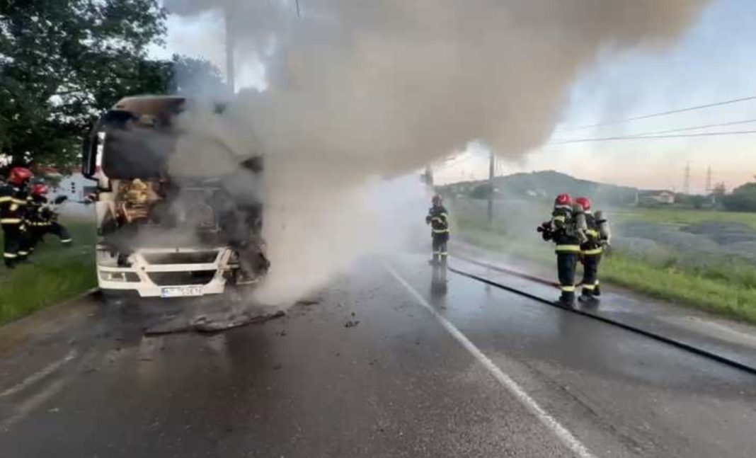Truck on fire on a wet road with thick smoke, firefighters in turnout gear use hoses to extinguish the blaze.