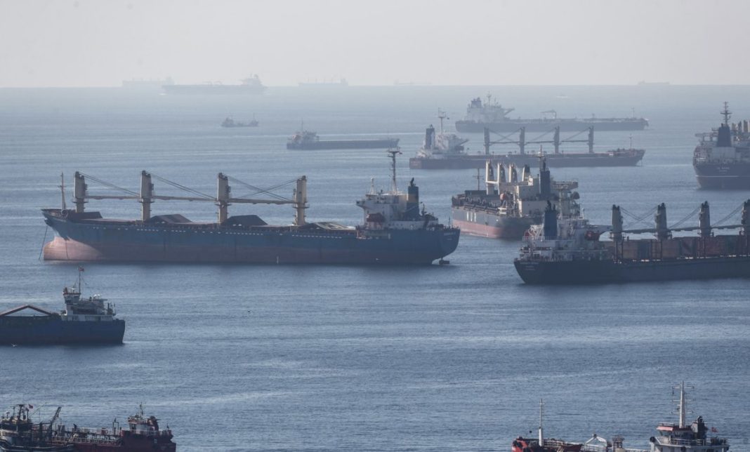 Busy sea scene with many large cargo ships and tankers anchored or moving near a harbor.