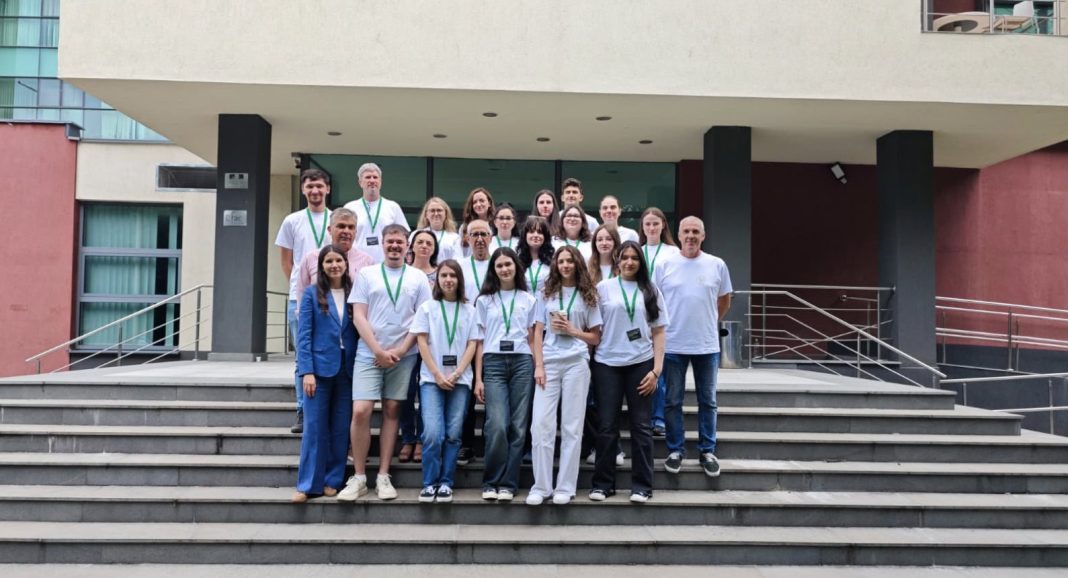 Group of about 25 people in white shirts and green lanyards posing on steps outside a modern building.